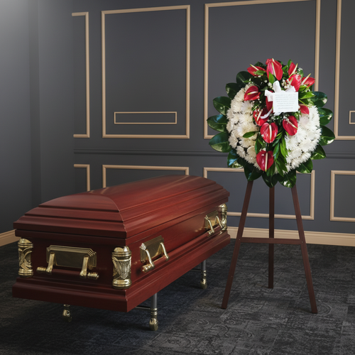 Ataúd de madera barnizada con herrajes dorados junto a una corona fúnebre de flores blancas y rojas sobre caballete en una sala interior de paredes grises