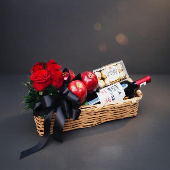 Arreglo ANGELO: Cesta Elegante con Rosas Rojas, Vino y Chocolates Arreglo ANGELO: Elegante cesta de mimbre con rosas rojas frescas, manzanas rojas, botella de vino tinto Finca Las Moras y caj