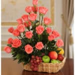 Elegante cesta de regalo con rosas salmón frescas, uvas rojas, manzanas verdes y rojas, peras y limón, ideal para ecommerce.