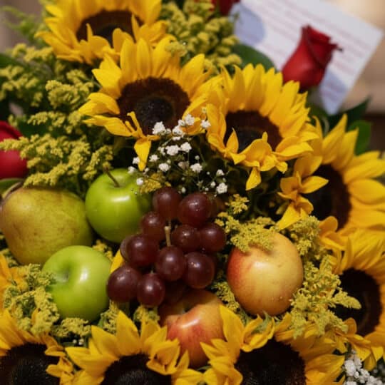 Primer plano extremo de un Arreglo Floral Dorado con girasoles vibrantes, manzanas verdes y rojas, peras, uvas rojas y sutile
