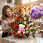 Mujer elegante admira un arreglo floral exótico con rosas rojas y rosadas, aves del paraíso, un oso de peluche y un globo de