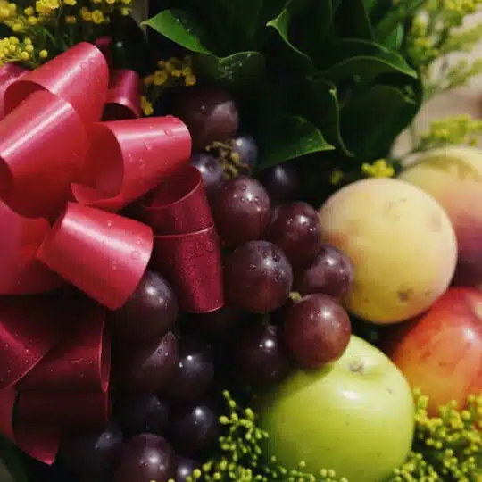 Primer plano extremo de un arreglo floral con frutas salak, uvas rojas, manzanas verdes y duraznos, destacando texturas y got