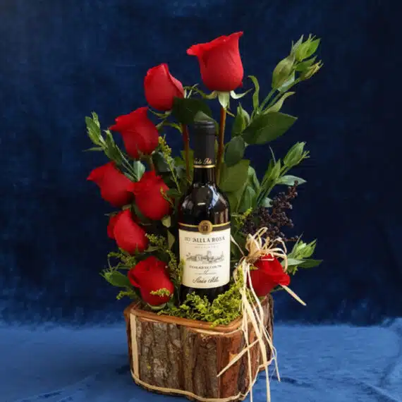 Arreglo floral VERITA con rosas rojas frescas y una botella de vino tinto, presentado en una base de madera rústica, ideal pa