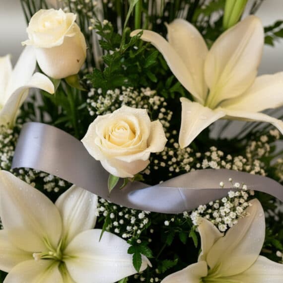 Fotografía macro premium del Arreglo Fúnebre Descanso Eterno, mostrando rosas y lirios blancos con rocío, follaje verde y una