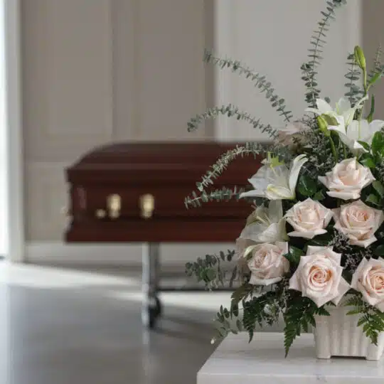 Arreglo floral fúnebre Inmortal con rosas pálidas, lirios blancos y eucalipto, en primer plano en una sala de velación modern
