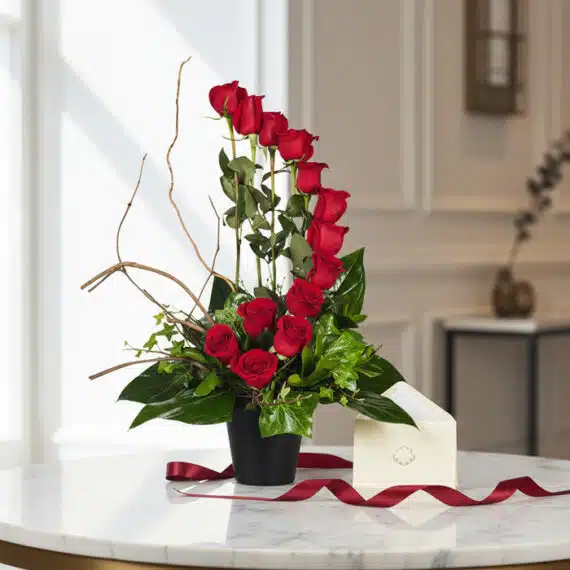 Arreglo floral GIANNA con 13 rosas rojas en jarrón negro, tarjeta de regalo y cinta satinada sobre mesa de mármol. Ideal para