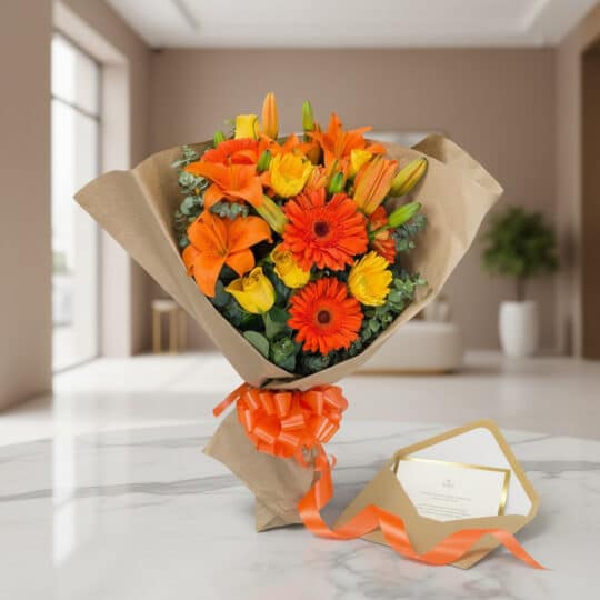Bouquet LIRICA con lirios naranjas, gerberas y rosas amarillas, envuelto en papel kraft con cinta naranja y tarjeta de regalo
