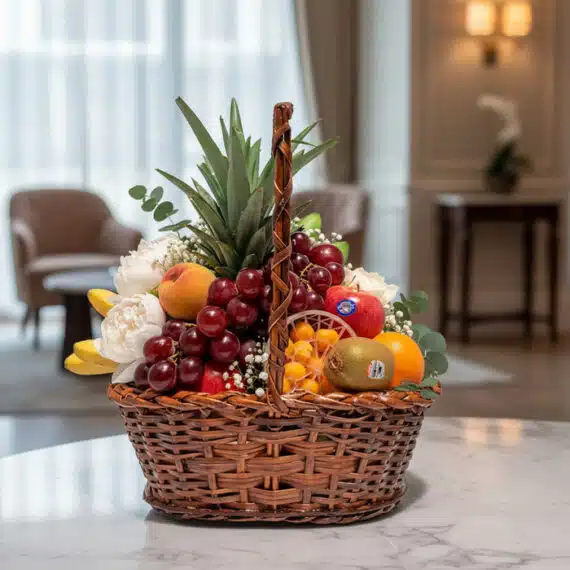 Canasta con Frutas Hydra: El Regalo Perfecto para Cualquier Ocasión Canasta de mimbre con piña, uvas rojas, manzanas, duraznos, kiwis, naranjas y plátanos, con flores blancas y eucalipto, sobre