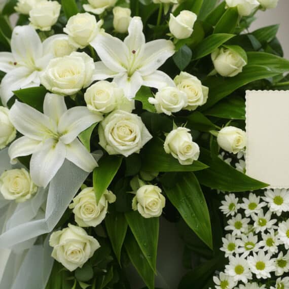 Corona fúnebre Legado Jacob con rosas blancas, lirios y margaritas, rocío sutil, cinta satinada y sobre de condolencias en un