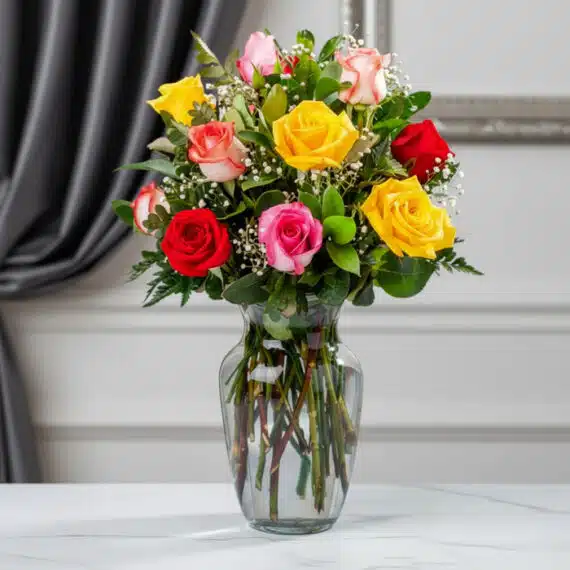 Jarrón con 12 Rosas Multicolor: Frescura y Elegancia para Regalar Jarrón de cristal transparente con un ramo de 12 rosas de colores variados: rojas, amarillas, rosas y blancas, con follaje ve