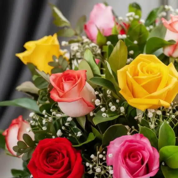 Primer plano extremo de un jarrón con 12 rosas multicolor, mostrando texturas hiperrealistas, gotas de rocío sutiles y colore