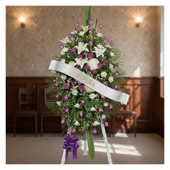 Pedestal Fúnebre Esteban: Elegancia Floral con Lirios y Rosas Pedestal fúnebre Esteban con arreglo floral de lirios blancos, rosas moradas y follaje verde, banda blanca con nombre 'Esteba