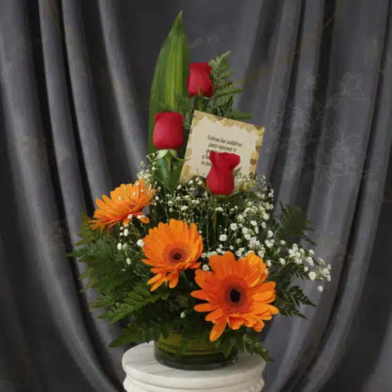 Solitario Tu Recuerdo: Elegante Arreglo Floral con Rosas y Gerberas Arreglo floral 'Solitario Tu Recuerdo' con tres rosas rojas, tres gerberas naranjas, follaje verde y flores blancas pequeñas,